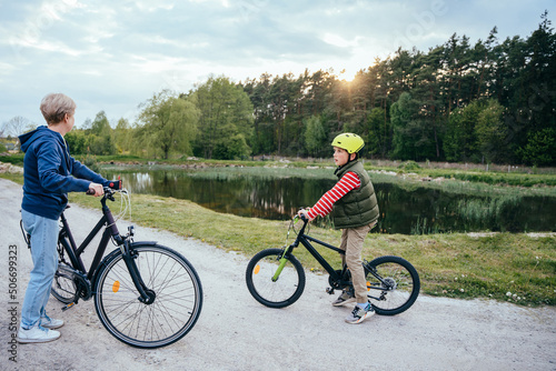 Fototapeta Naklejka Na Ścianę i Meble -  Active senior grandmother and child boy riding bikes in nature with lake on background.