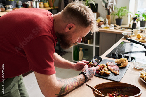 Fototapeta Naklejka Na Ścianę i Meble -  Modern male food blogger using smartphone to take pictures of beef steak with potatoes and bread