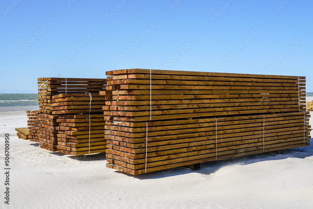 Large stacks of impregnated brown pine wood boards by the sea on a sandy beach Large stacks of impregnated brown pine wood boards by the sea on a sandy beach