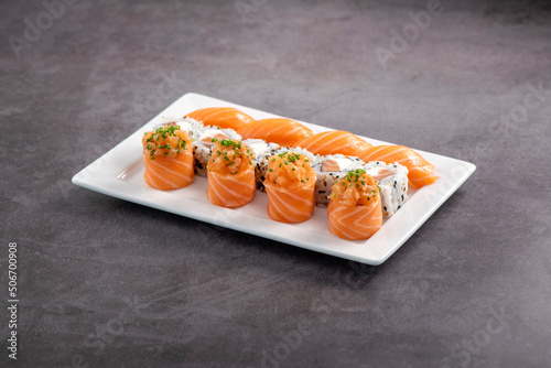 Fresh made sushi mix. Different kinks of salmon sushi served on white plate. Studio shoot on slated background.