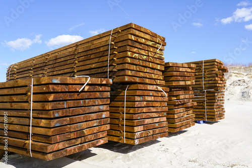 Large stacks of impregnated brown pine wood boards by the sea on a sandy beach