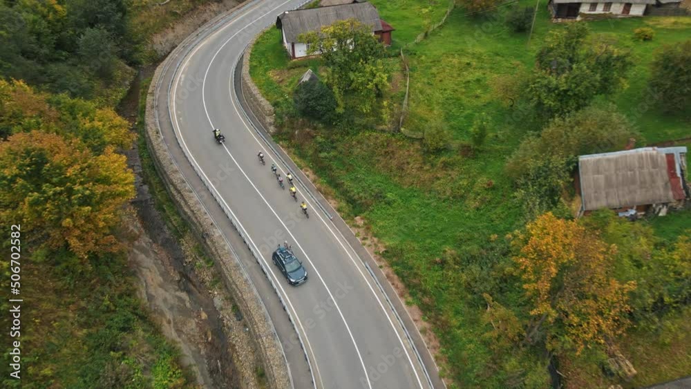Close up aerial view people riding bicycles on road near village. Lots of participants of sports competition. Concept of sports and healthy lifestyle. Drone. Slow motion Close up aerial view people riding bicycles on road near village. Lots of participants of sports competition. Concept of sports and healthy lifestyle. Drone. Slow motion