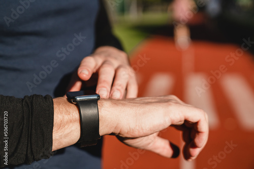 Fitness smart watch. Male runner athlete sportsman checking time, physical activity, running distance on armband while training jogging in stadium.