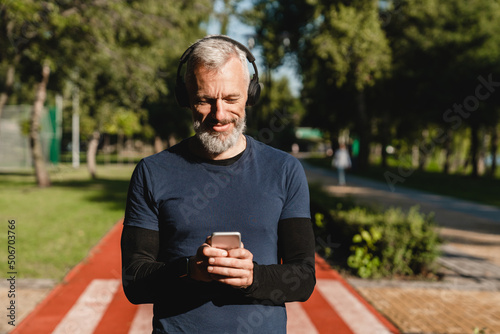 Closeup cropped portrait of a male caucasian mature athlete sportsman runner choosing sound track on smart phone listening to the music while jogging on stadium in the morning.