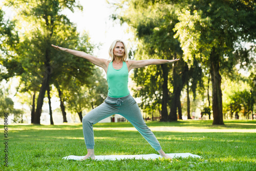 Mature caucasian fit woman in sporty clothes training, doing workout on fitness mat in public park. Yoga class outdoors. Healthy lifestyle