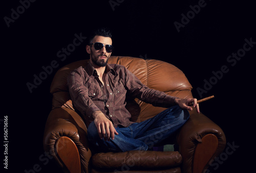 Man with glasses sitting with habano in brown leather armchair photo