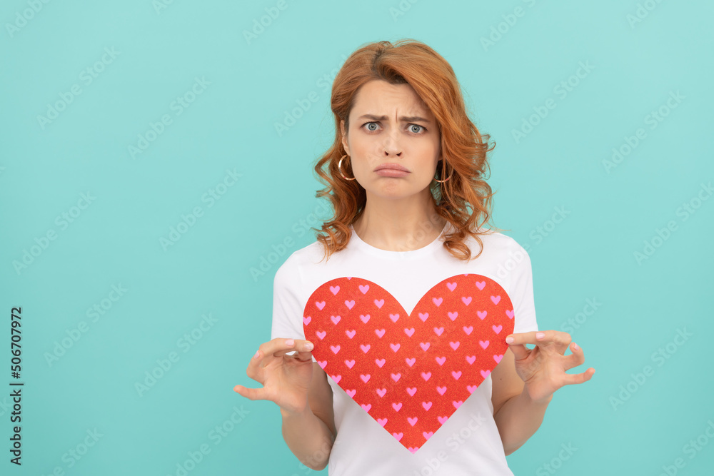 confused redhead girl hold red heart on blue background confused redhead girl hold red heart on blue background