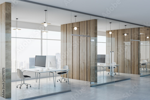 Side view on modern spacious coworking office with wooden wall partitions, modern computers on minimalistic style tables, concrete floor and glass wall instead windows. 3D rendering