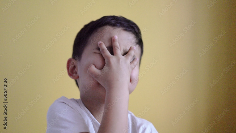 Cute boy smiling and covering his face on colour background Cute boy smiling and covering his face on colour background
