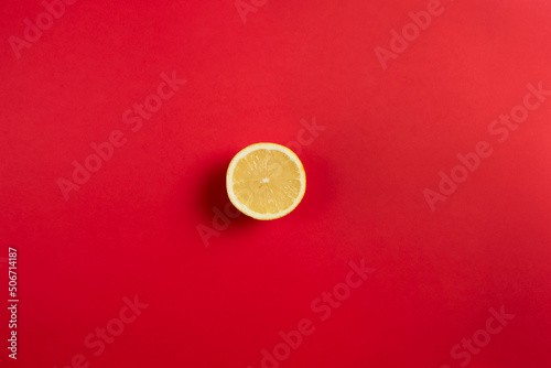 Bright red background with half a lemon in the center of the image. Flat top view