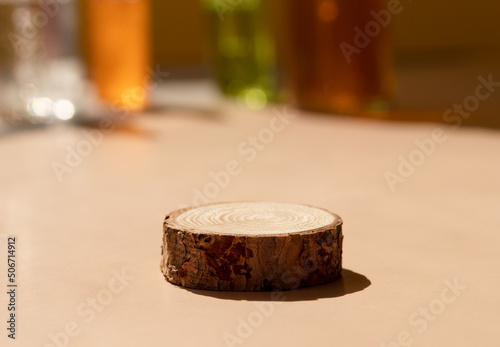 Wooden podium on beige background with blurred cosmetic bottles behind. Soft focus. A platform for natural products, perfume testers or samples. Tray mockup in the sunlight. Front view