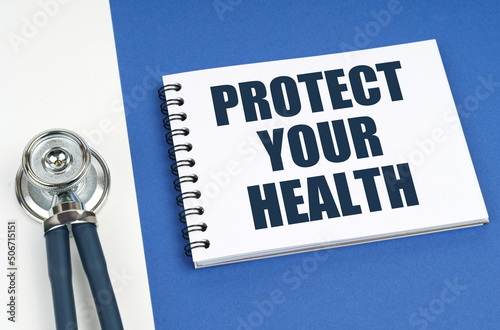 On a blue-white surface lies a stethoscope and a notepad with the inscription - PROTECT YOUR HEALTH