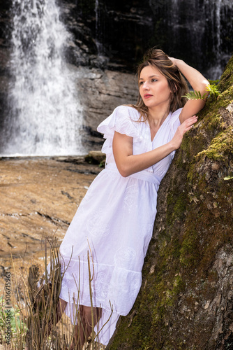 blonde woman in a white dress leaning on a tree in a waterfall