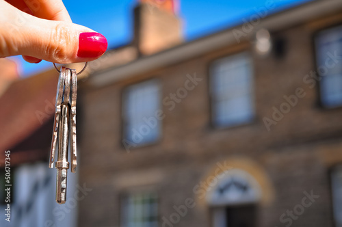 Woman's hand holding metal keys on blurred background with house  photo