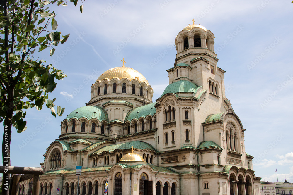 Alexander Nevsky facade cathedral in the center of Sofia, capital city of Bulgaria, on a sunny day, with a tree and blue sky for a tourist walk - beautiful orthodox symbol for a travel around balkans
