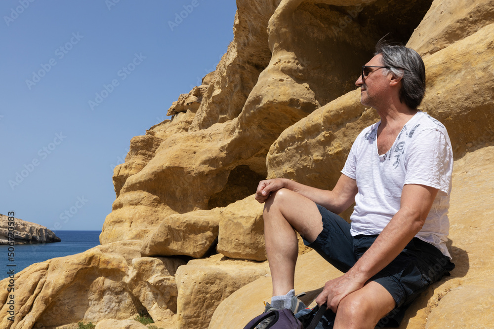 middle-aged man sits on yellow rocks in Matala and looks into the distance, Greece middle-aged man sits on yellow rocks in Matala and looks into the distance, Greece