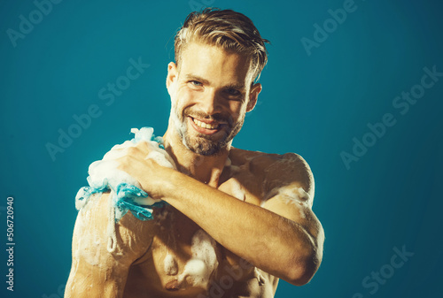 Smiling man washing body with moisturizing gel and washcloth taking shower. Morning routine. Spa. photo