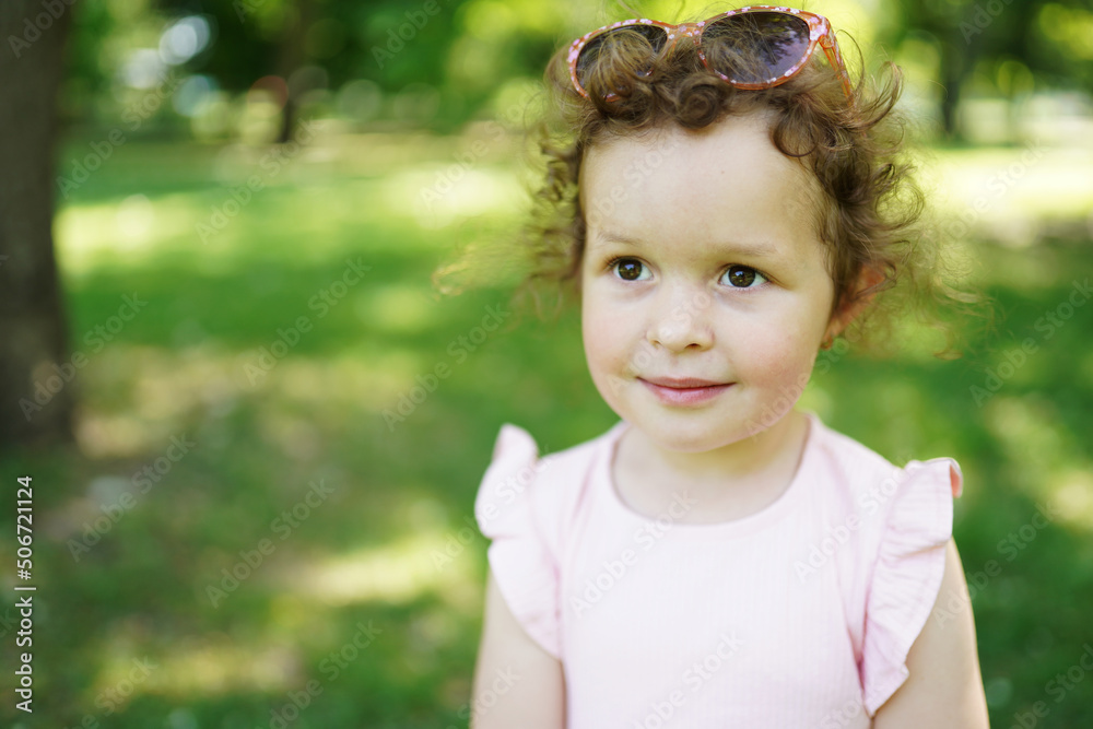 Child girl with beautiful curly hair in pink dress in amazing sunset light. Portrait of pretty female kid at nature