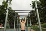 Pull up strength training exercise - fitness man working out his arm muscles on outdoor beach gym doing chin-ups, pull-ups as part of a crossfit workout routine.