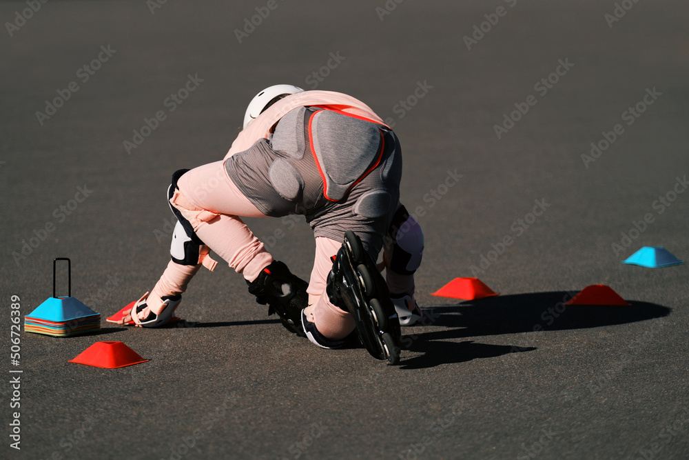 Obraz premium A girl roller skater in protection gets up on roller skates after a fall. Failure in training.