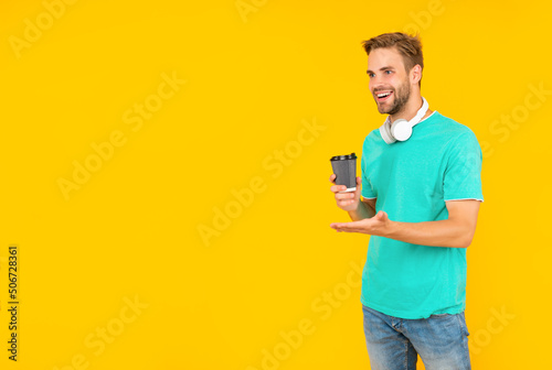 smiling man in blue shirt wear earphones and hold coffee cup on yellow background, modern education