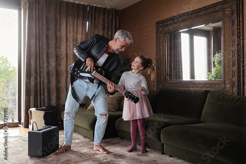 Father rock guitarist having fun and dancing with his little daughter at home.