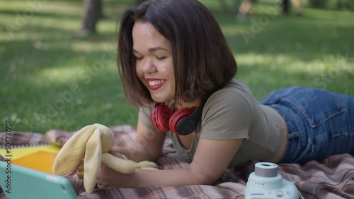 Relaxed positive little woman playing with toy lying on blanket in spring summer park. Portrait of joyful happy Caucasian person with dwarfism enjoying leisure outdoors. Slow motion photo