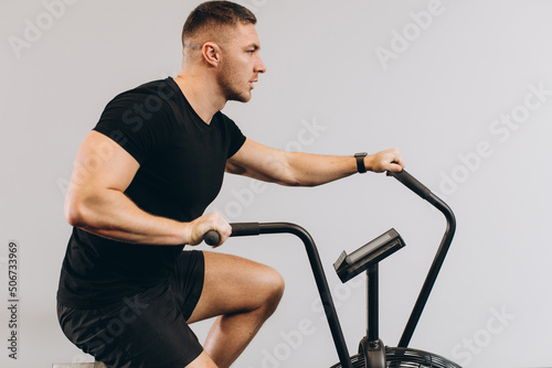 Strong man using air bike for cardio workout at cross training gym.