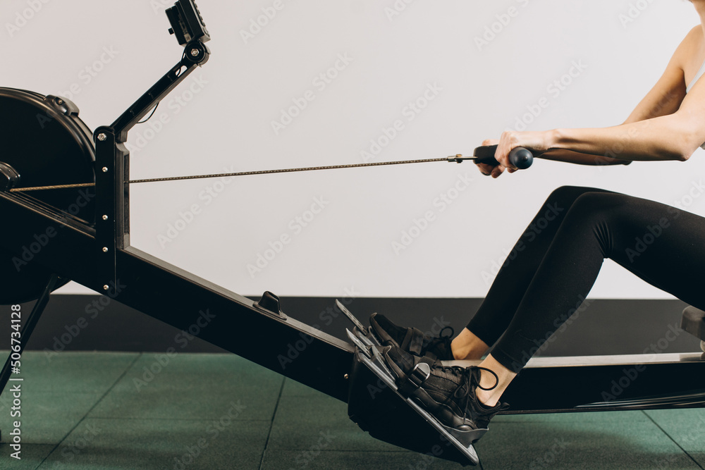 Woman exercising on rowing machine, part of circuit training warmup cardio session - obrazy, fototapety, plakaty 
