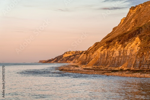 sunset over the sea, pastel colours of the sky, orange lights, mountains and beach