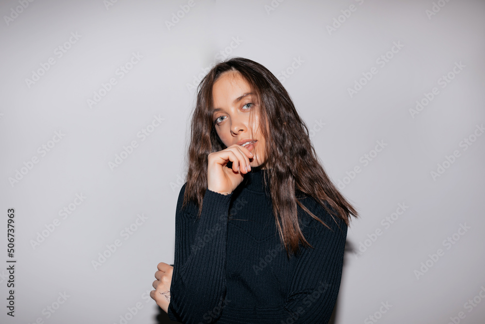 Stylish trendy girl with wavy long hair wearing black shirt touching her chin and looking at camera over isolated background. Indoor portrait of attractive lovely woman Stylish trendy girl with wavy long hair wearing black shirt touching her chin and looking at camera over isolated background. Indoor portrait of attractive lovely woman