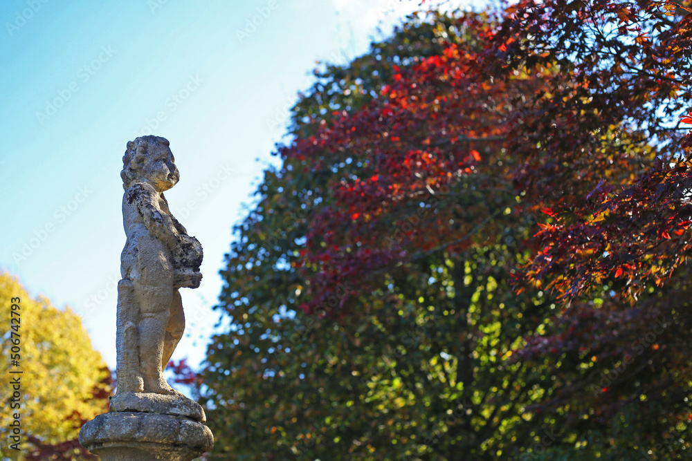 Fountain boy statue in autumn maple tree leaf landscape in Australia, red, green colours with sunlight and blue sky, close up seletive focus view Fountain boy statue in autumn maple tree leaf landscape in Australia, red, green colours with sunlight and blue sky, close up seletive focus view