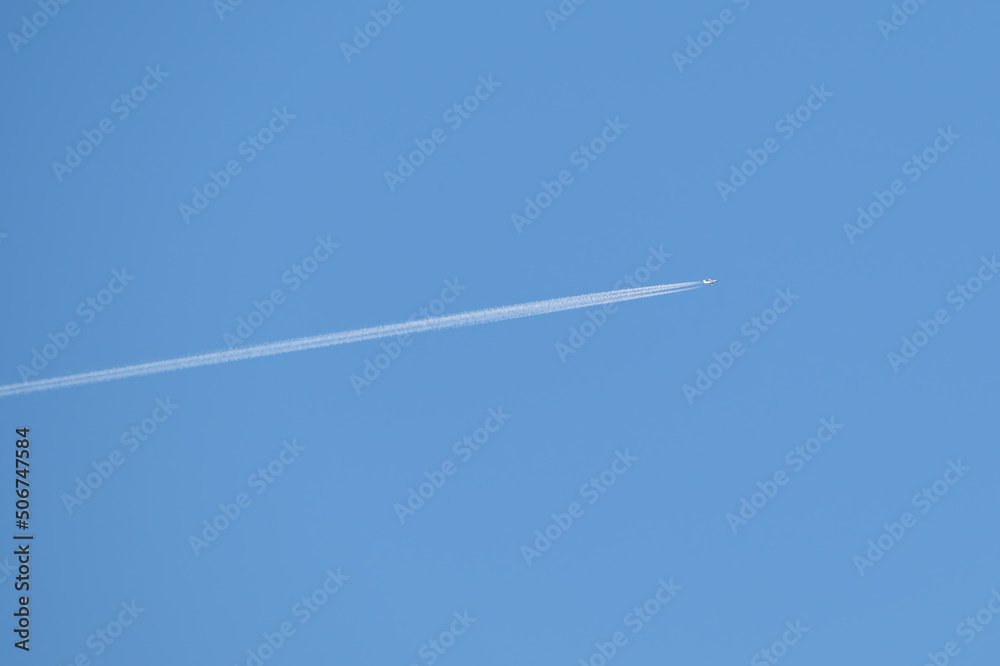 Distant passenger jet plane flying on high altitude on clear blue sky leaving white smoke trace of contrail behind. Air transportation concept