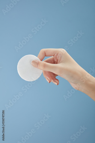 Topview of hand model using makeup remover on cotton pad in blue background for cosmetic advertising	
