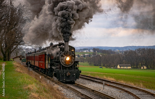 An Antique Steam Passenger Train Traveling Thru Farmlands Puffing Lots of Smoke on a Cloudy Winter Day