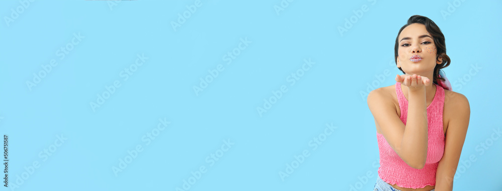 Attractive young woman with glitters on her face blowing kiss against light blue background with space for text Attractive young woman with glitters on her face blowing kiss against light blue background with space for text