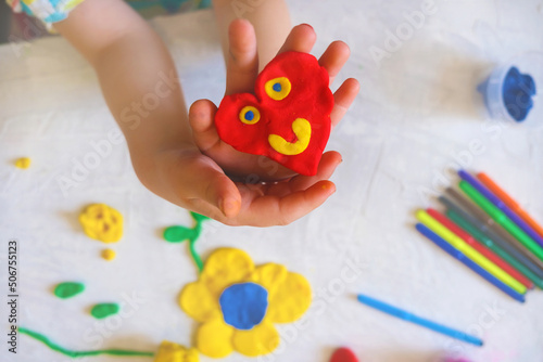 Hands of little girl making funny heart from colorful clay dough, plasticine, Home Education game with clay. Early development concept. Educational and entertaining classes with children