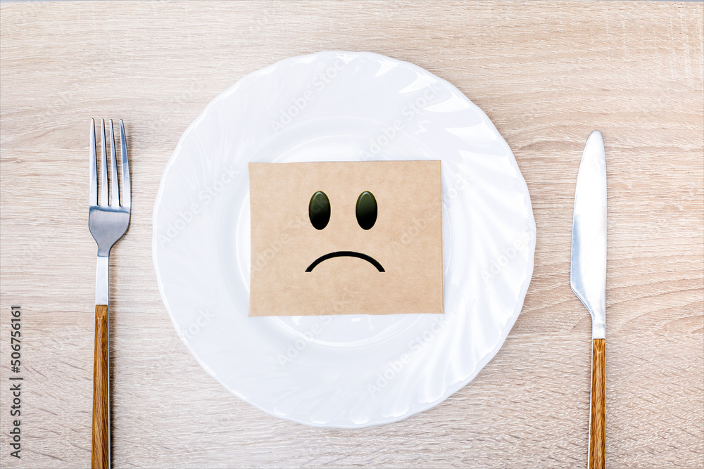 Label with a sad smiley face in a white plate. Crisis food, hungry ...