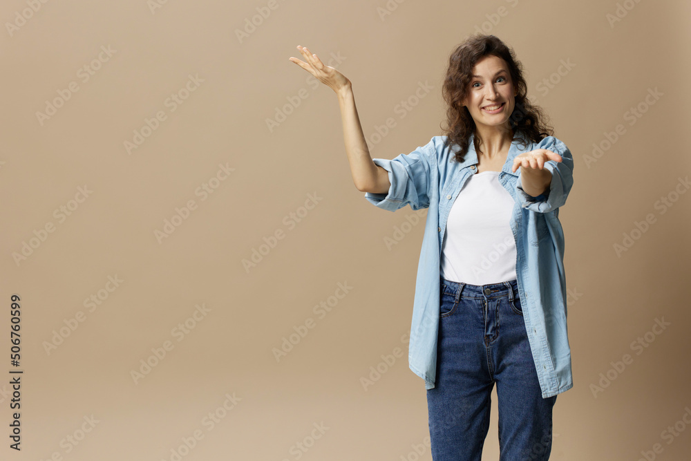 Excited happy cheerful curly beautiful female in jeans casual shirt point hand up at camera posing isolated on over beige pastel background. People Lifestyle emotions concept. Copy space Excited happy cheerful curly beautiful female in jeans casual shirt point hand up at camera posing isolated on over beige pastel background. People Lifestyle emotions concept. Copy space