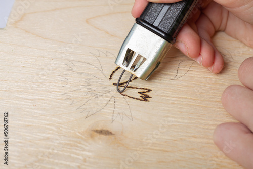 Burn out a drawing on a wooden board with an electric device with a scorcher