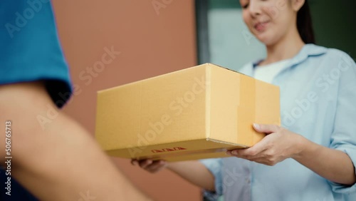 Close up parcel in hand of blue uniform delivery man to customer front of the house from shopping online with good service. Courier man delivering a cardboard box postal package to destination. photo