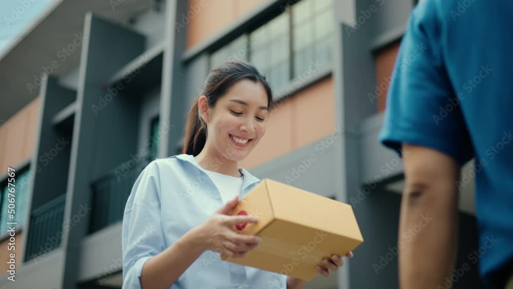 Beautiful Young Woman receiving parcel from blue uniform delivery man f the house with good service from shopping online. Courier man delivering a cardboard box postal package to destination. Beautiful Young Woman receiving parcel from blue uniform delivery man f the house with good service from shopping online. Courier man delivering a cardboard box postal package to destination.