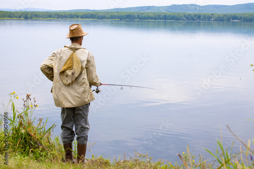 A fisherman is fishing with a line in the lake. Back view