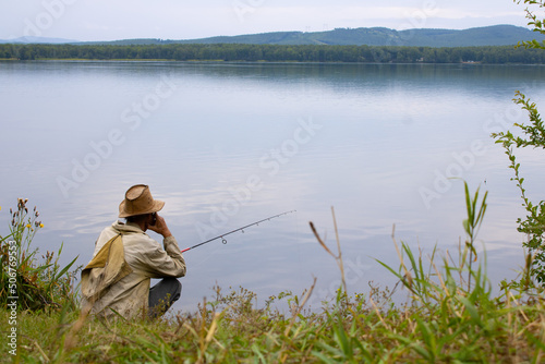 A fisherman sits by the lake and catches a fish with a line. Back view