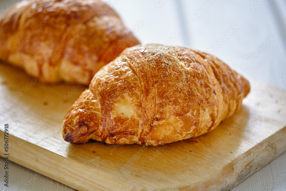 A crispy croissant with almond filling and hot black coffee on a wooden board on a light concrete table.