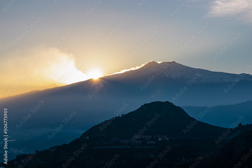 Panoramic view on silhouette of hills and coastal towns. Watching the beautiful sunset behind volcano Mount Etna near Castelmola, Taormina, Sicily, Italy, Europe, EU. Sun disappearing behind mountain