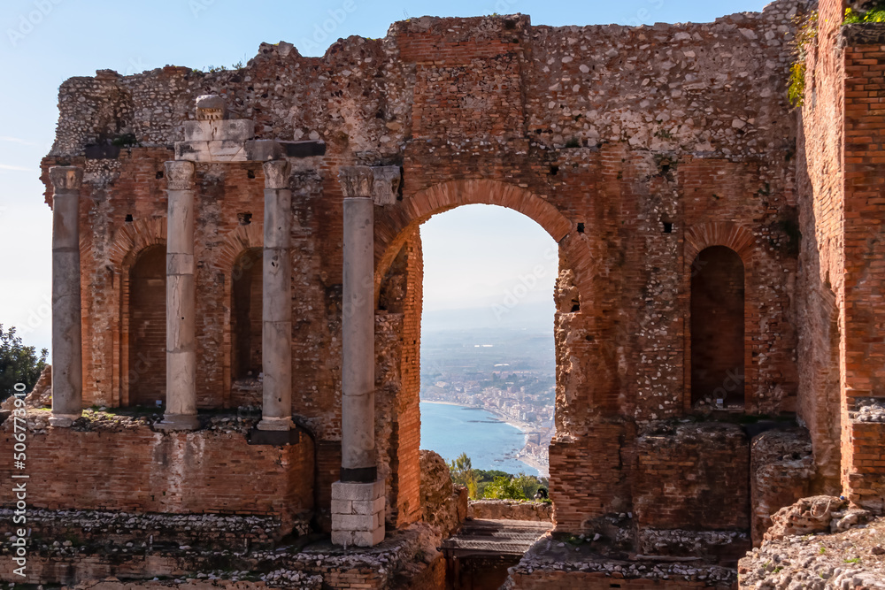 Panoramic view on the ruins of ancient Greek theater Taormina, island Sicily, Italy, Europe, EU. Looking through the red brick wall gate of the archeological ruins on the Mediterranean coastline