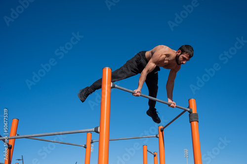 A man with a naked torso makes a balance on the horizontal bar. 