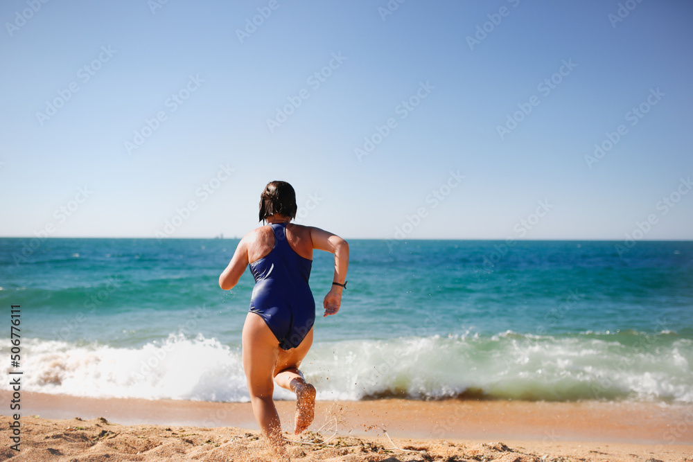 overweight teenager girl runs on beach to sea, child girl in one-piece swimsuit. Summer vacation by the sea