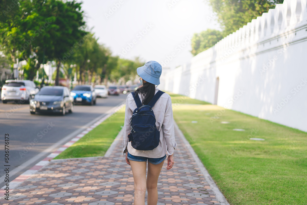 Rear view of young adult walking travel in the city wear blue bag and hat